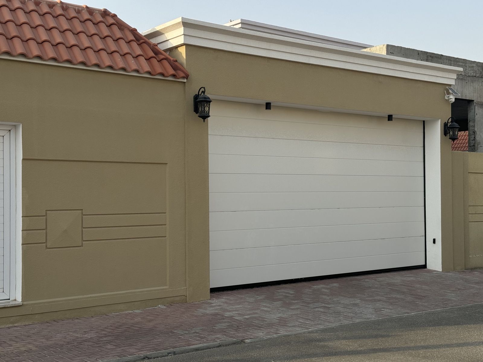White sectional garage door on a beige classic villa with terracotta roof tiles and lanterns