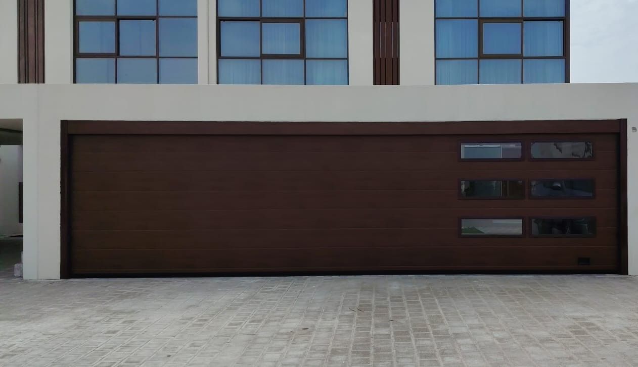 Dark wood-finish sectional garage door with rows of window inserts on a modern villa