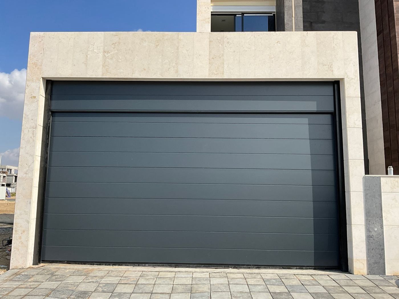 Dark grey (anthracite) sectional garage door in a travertine stone frame